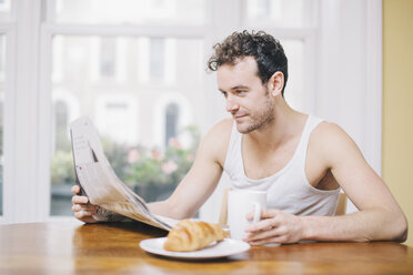 Young man reading newspaper at breakfast - CUF23319