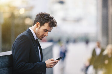 Businessman reading smartphone texts on city street - CUF23323