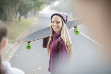 Lächelndes Teenager-Mädchen, das sich mit einem Freund auf dem Skateboard trifft - ZEF15600