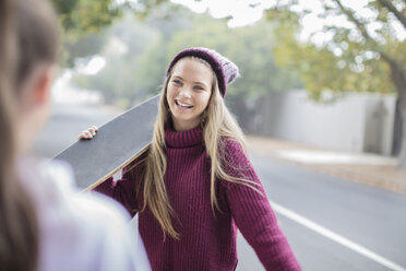 Lächelndes Teenager-Mädchen, das sich mit einem Freund auf dem Skateboard trifft - ZEF15601