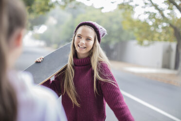 Smiling teenage girl holding skateboard meeting with friend - ZEF15601