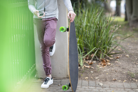 Nahaufnahme eines Jungen, der ein Skateboard hält und ein Mobiltelefon benutzt, lizenzfreies Stockfoto