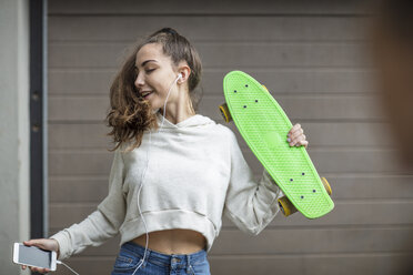 Unbekümmertes Teenager-Mädchen tanzt, während sie ein Skateboard hält und Musik hört - ZEF15612