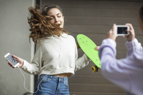 Ein Freund fotografiert ein sorgloses Teenager-Mädchen, das tanzt, während es ein Skateboard hält und Musik hört - ZEF15613