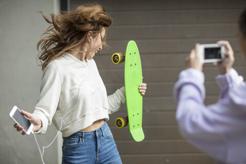 Ein Freund fotografiert ein sorgloses Teenager-Mädchen, das tanzt, während es ein Skateboard hält und Musik hört, lizenzfreies Stockfoto