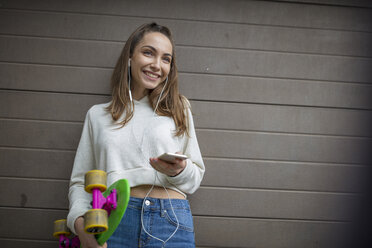 Lächelndes Teenager-Mädchen mit Handy, Kopfhörern und Skateboard - ZEF15615