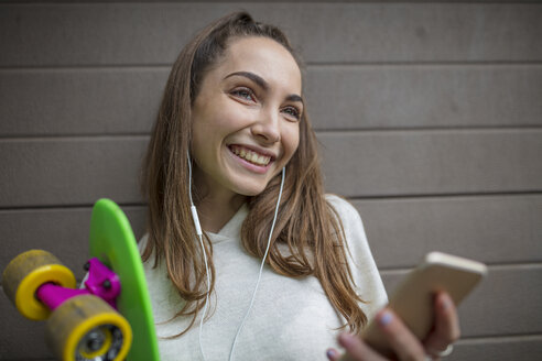 Porträt eines lächelnden Teenagers mit Mobiltelefon, Kopfhörern und Skateboard - ZEF15616