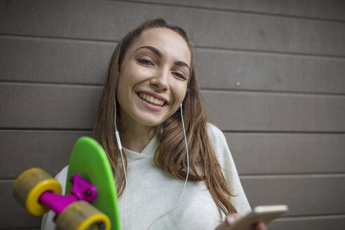 Porträt eines lächelnden Teenagers mit Mobiltelefon, Kopfhörern und Skateboard - ZEF15617