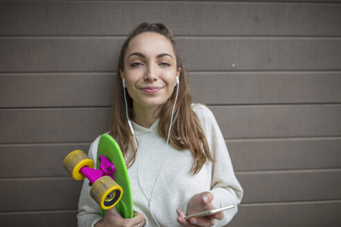 Porträt eines lächelnden Teenagers mit Mobiltelefon, Kopfhörern und Skateboard - ZEF15618