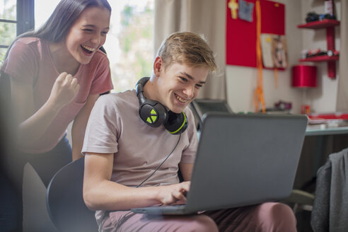 Glückliches Mädchen im Teenageralter, das einen Jungen beobachtet, der einen Laptop benutzt - ZEF15621