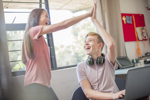 Glückliches Teenager-Mädchen und Junge mit Laptop, die sich die Hände reichen, lizenzfreies Stockfoto
