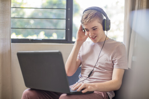 Lächelnder Junge mit Kopfhörern und Laptop, lizenzfreies Stockfoto