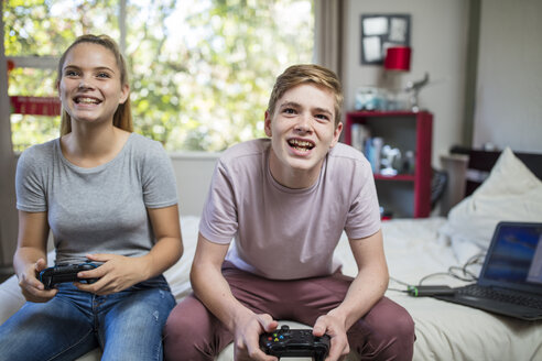 Glückliches Teenager-Mädchen und Junge sitzen auf dem Bett und spielen ein Videospiel - ZEF15643