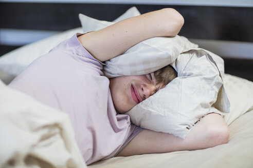 Boy lying in bed holding pillow over his head - ZEF15645