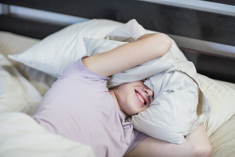 Boy lying in bed holding pillow over his head stock photo