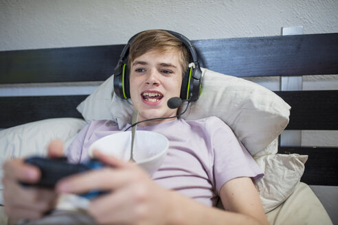 Junge liegt im Bett und spielt ein Videospiel - ZEF15647