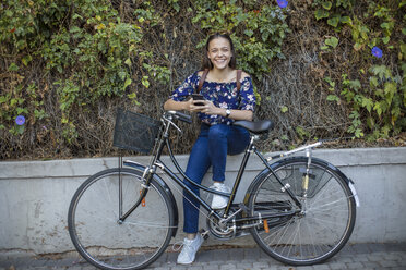 Portrait of smiling teenage girl with cell phone and bicycle - ZEF15653