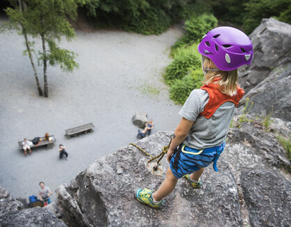 Junge mit Kletterhelm steht auf einem Felsen und schaut nach unten - CUF23364