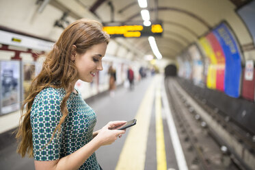 Seitenansicht einer Frau auf einem Bahnsteig, die auf ihr Smartphone schaut - CUF23387