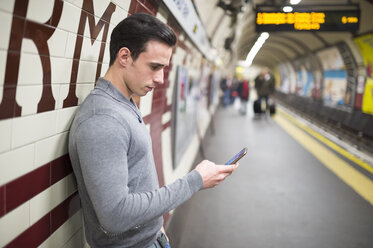 Seitenansicht eines Mannes auf einem Bahnsteig, der auf sein Smartphone schaut - CUF23388