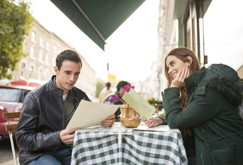 Paar in einem Straßencafé betrachtet lächelnd die Speisekarte - CUF23389