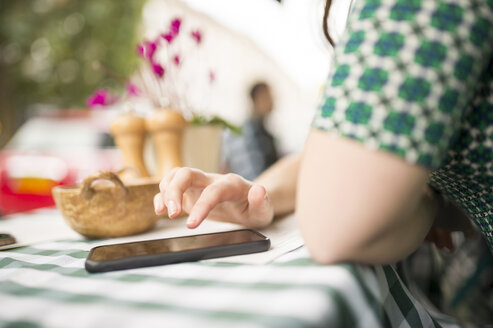 Beschnittene Ansicht einer Frau in einem Straßencafé, die ein Smartphone benutzt - CUF23393