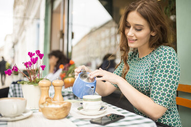Frau im Straßencafé schenkt aus einer Teekanne ein - CUF23395