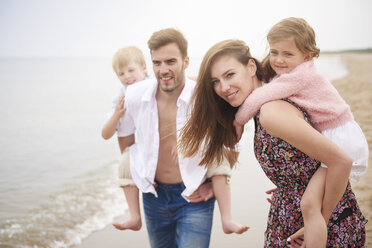 Parents giving children piggybacks on beach - CUF23414