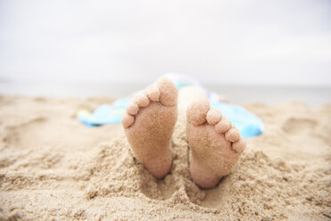 Kind am Sandstrand liegend, Blick von den Füßen - CUF23420
