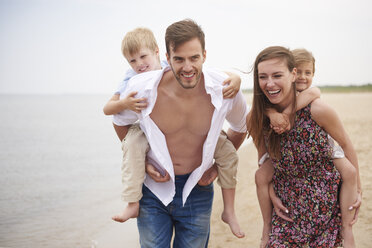 Parents giving children piggybacks on beach - CUF23430
