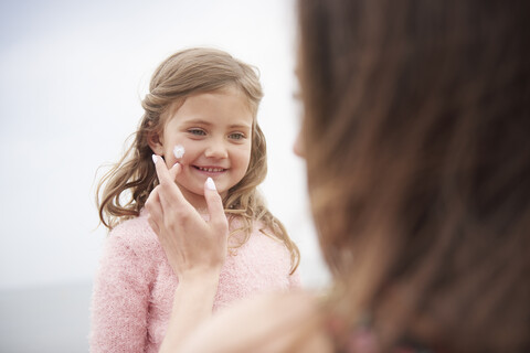 Mutter trägt Sonnencreme auf die Wange ihrer Tochter auf, lizenzfreies Stockfoto