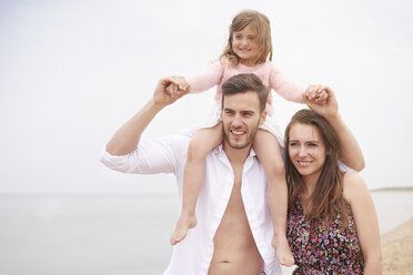 Family walking on beach, daughter sitting on father's shoulders - CUF23440