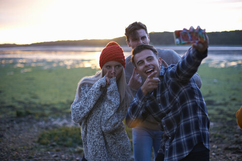 Drei junge Erwachsene machen ein Smartphone-Selfie bei Sonnenuntergang am Meer - CUF23444