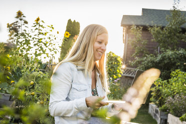 Woman looking at laptop in community garden, Vancouver, Canada - CUF23451