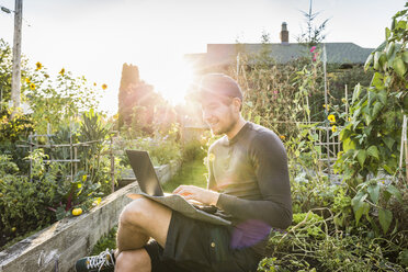 Man typing on laptop in sunlit community garden, Vancouver, Canada - CUF23452