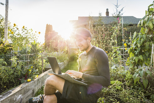 Mann tippt auf einem Laptop im sonnigen Gemeinschaftsgarten, Vancouver, Kanada - CUF23452