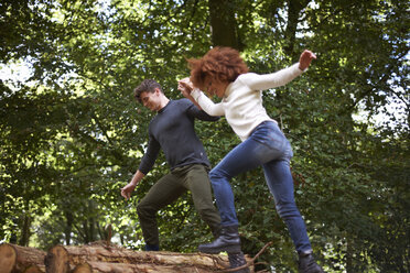 Paar im Wald hält sich an den Händen und balanciert auf einem umgestürzten Baum - CUF23487