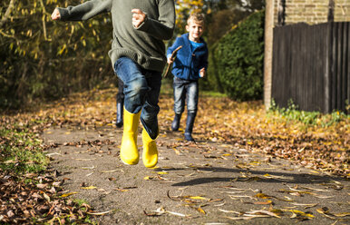 Three boys, running along pathway in autumn, low section - CUF23513