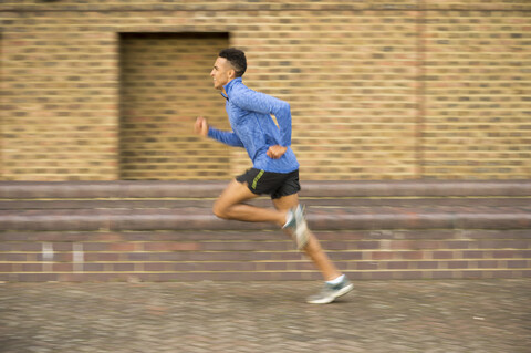 Man running past brick wall, Wapping, London, UK stock photo