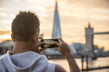 Mann am Flussufer, der die Tower Bridge und The Shard fotografiert, Wapping, London, UK - CUF23525