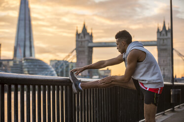 Mann, der sich gegen ein Geländer streckt, Tower Bridge und The Shard im Hintergrund, Wapping, London, UK - CUF23526