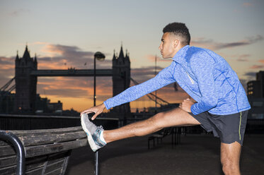 Man stretching by riverside, Tower Bridge in background, Wapping, London, UK - CUF23528