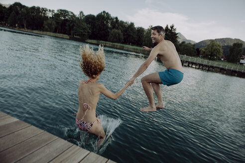 Glückliches Paar springt Hand in Hand in den Badesee - JLOF00044