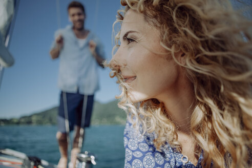 Lächelnde Frau auf einem Segelboot mit Mann im Hintergrund - JLOF00065