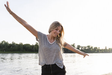 Young woman walking on riverside, raised arms - UUF14022