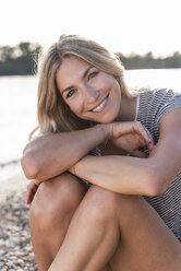 Young blonde woman wearing shorts sitting on riverbank, putting on