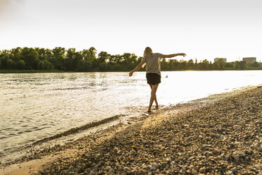 Young woman walking barefoot on riverside - UUF14030
