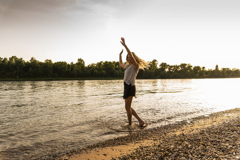 Junge Frau läuft abends barfuß am Flussufer - UUF14032