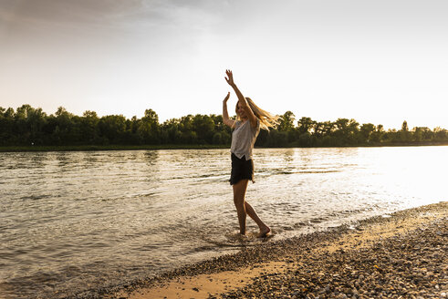 Young woman walking barefoot on riverside in the evening - UUF14032