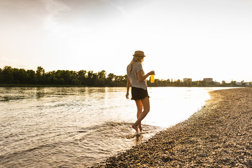 Young woman walking barefoot on riverside in the evening - UUF14035